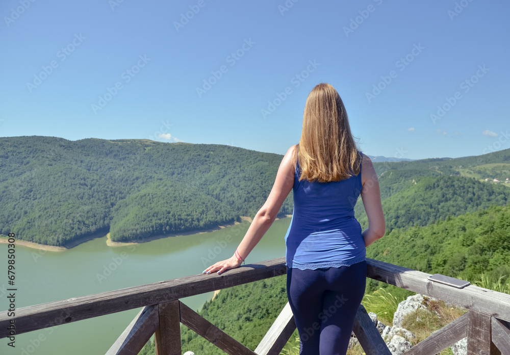 Naklejka premium Rear view at happy free woman enjoying beautiful view of mountains and lake
