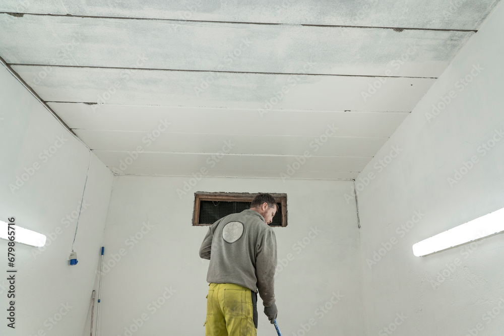 Skilled Worker in Branded Attire Transforms Spacious Room or Garage with Expert Painting.