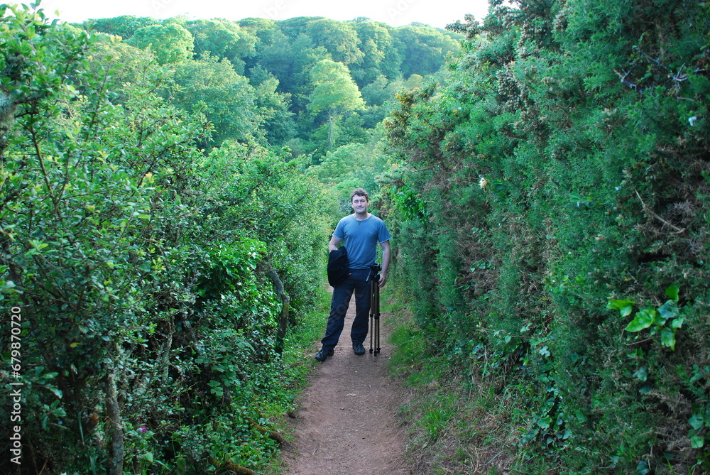 Man is standing on a footpath in a lush green environment 