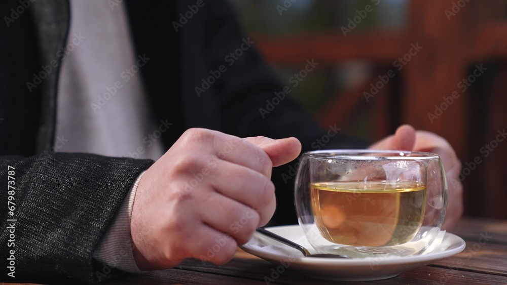 Man enjoys drinking hot tea in cafe gazebo looking to side in cold weather