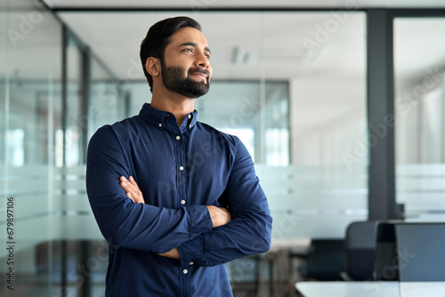 Confident Indian business man leader looking aside standing in office. Smiling professional businessman manager executive, male entrepreneur from India thinking of future career and financial success.