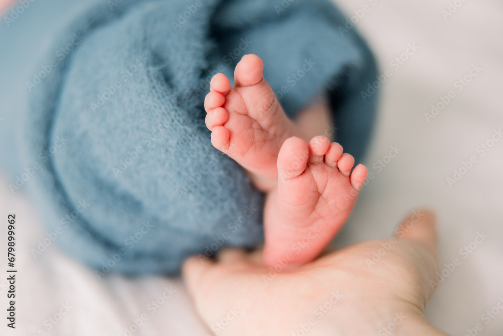 A baby is wrapped up in a blue blanket, his newborn foot and toes are sticking out. - obrazy, fototapety, plakaty 