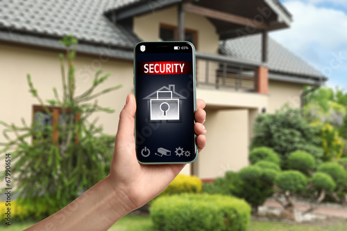 Woman using home security system application on smartphone outdoors, closeup