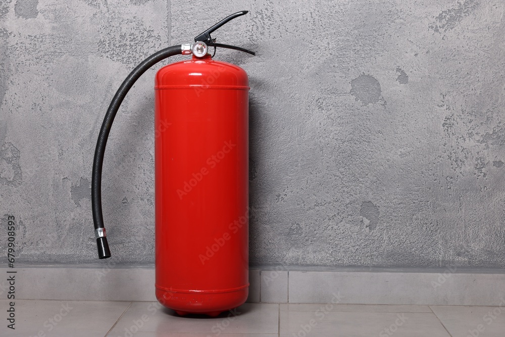 Red fire extinguisher near grey wall, space for text Red fire extinguisher near grey wall, space for text