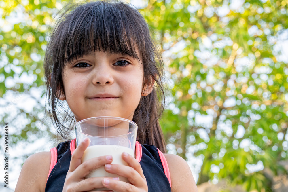 Close-up portrait of her. She drinks a glass of cold milk after playing outside her house. Close-up portrait of her. She drinks a glass of cold milk after playing outside her house.