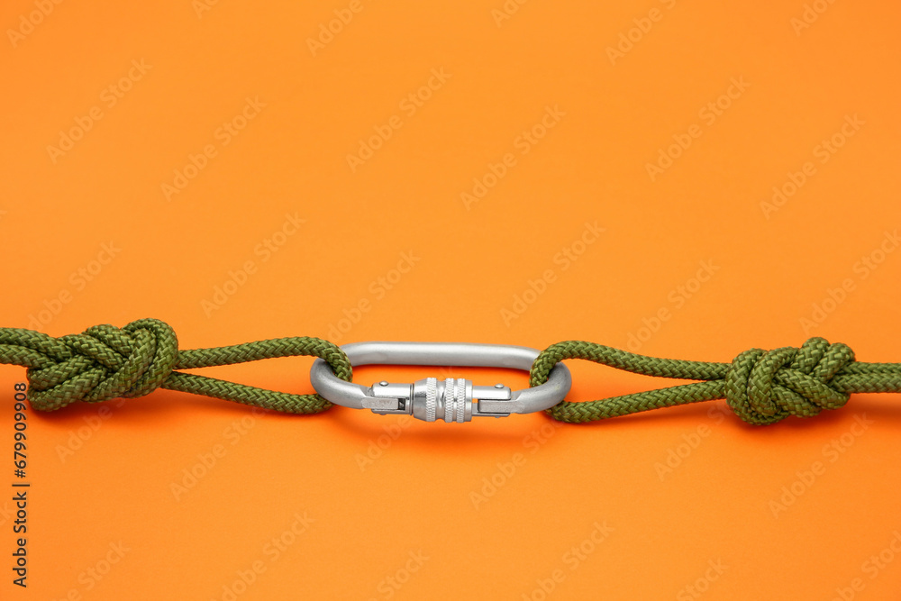 One metal carabiner with ropes on orange background, space for text