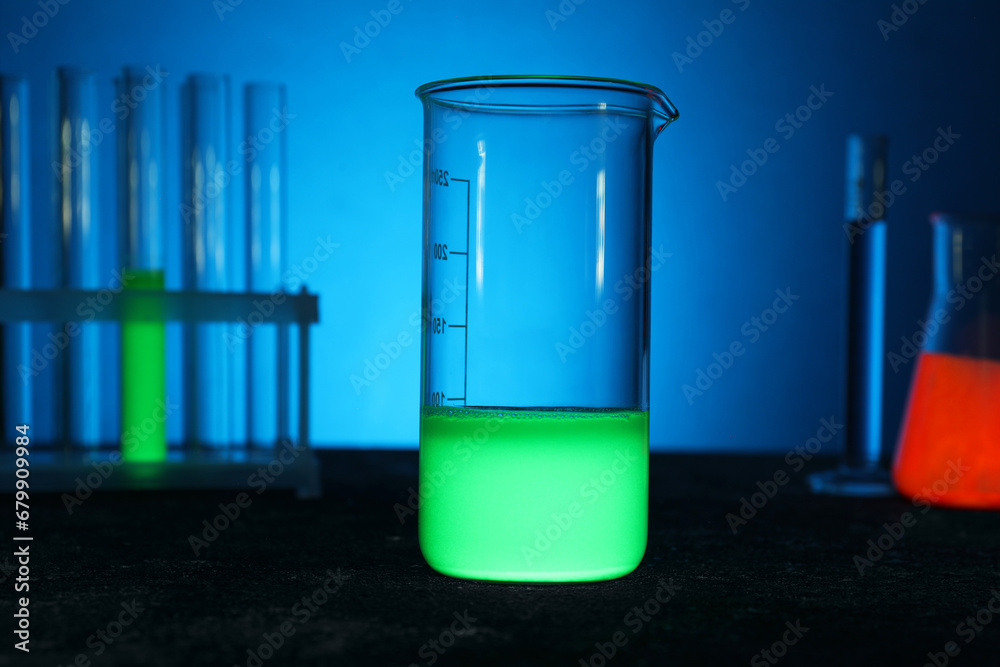 Laboratory beaker with luminous liquid on table against blue background