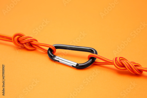 One metal carabiner with ropes on orange background, closeup