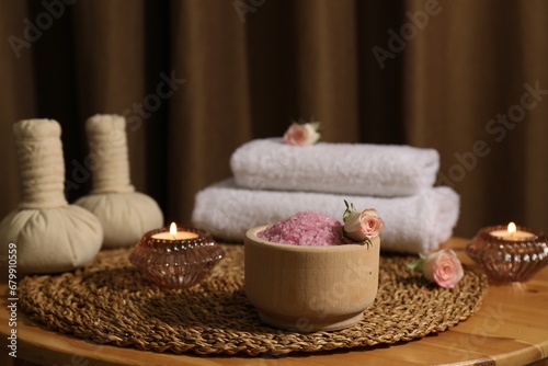 Bowl of pink sea salt  roses  burning candles and towels on wooden table