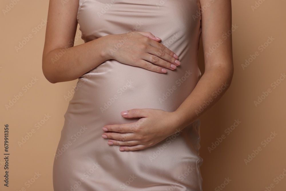 Pregnant woman in dress on beige background, closeup