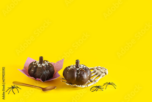 Fototapeta Naklejka Na Ścianę i Meble -  Delicious chocolate cakes, skeleton hand and spoon for Halloween celebration on yellow background