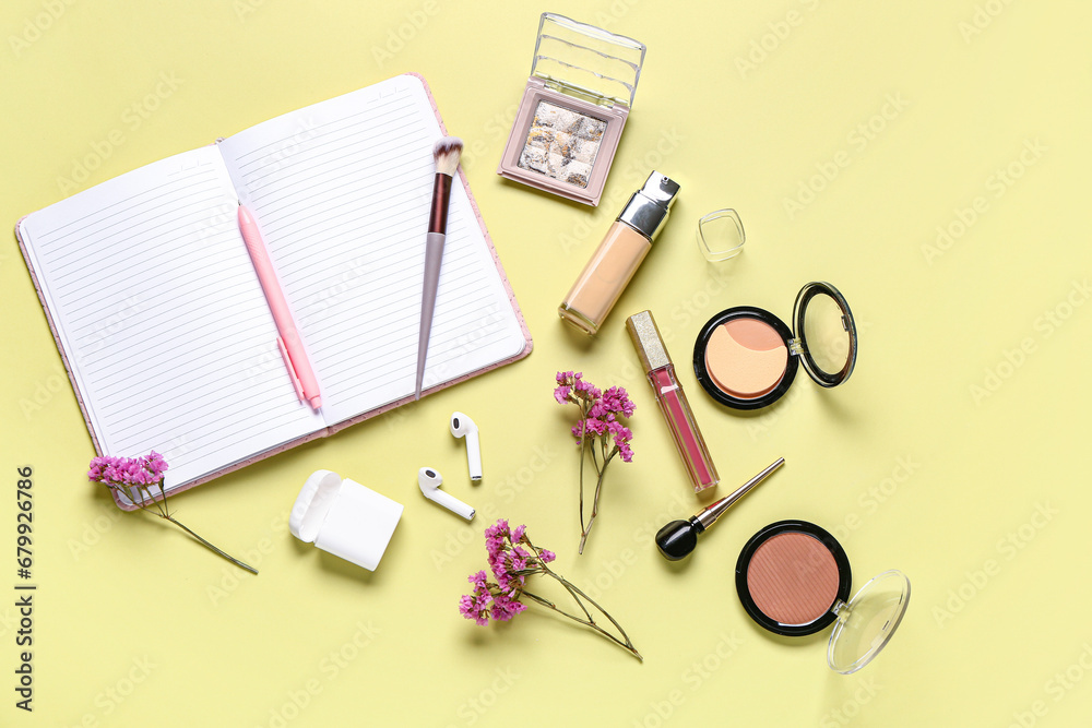 Composition with makeup cosmetics, modern earphones, beautiful flowers and notebook on yellow background Composition with makeup cosmetics, modern earphones, beautiful flowers and notebook on yellow background