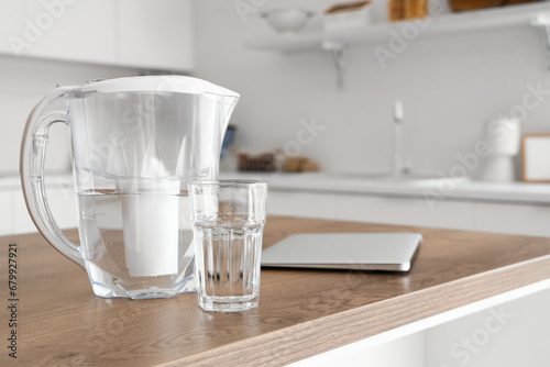 Water filter pitcher, glass and laptop on kitchen table