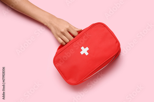 Female hand with first aid kit on pink background