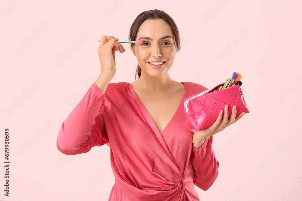 Beautiful young woman with cosmetic bag full of makeup products and brush on pink background Beautiful young woman with cosmetic bag full of makeup products and brush on pink background