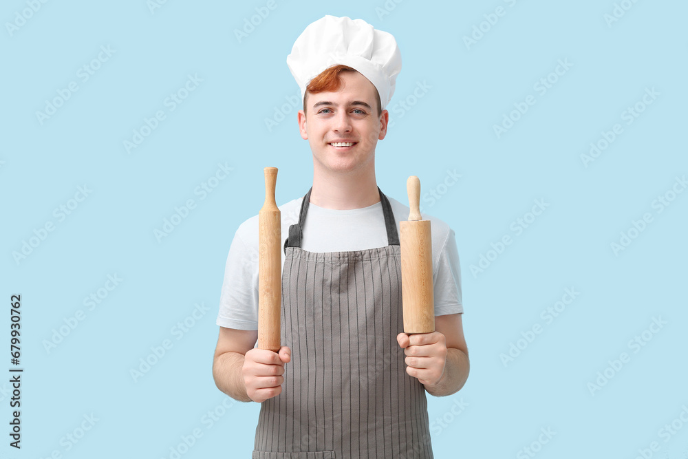 Male confectioner in apron with rolling pins on blue background Male confectioner in apron with rolling pins on blue background