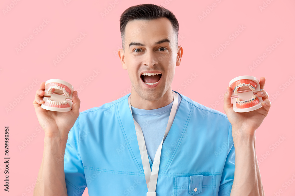 Male dentist holding jaw models with braces on pink background, closeup Male dentist holding jaw models with braces on pink background, closeup