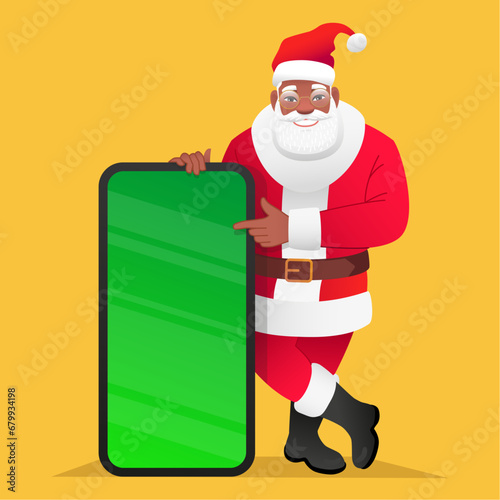 Black bearded Santa Claus leans on a large phone with a chroma key. African Santa points to the smartphone screen. Christmas concept for mobile app advertising.