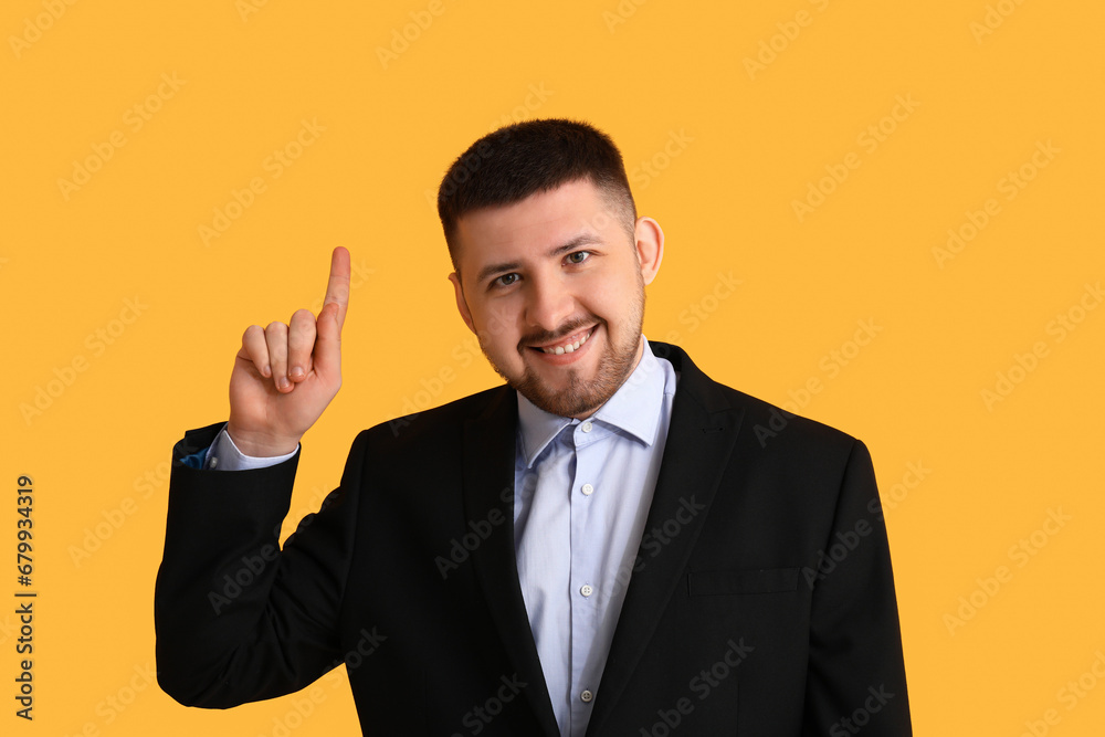 Young thoughtful businessman pointing at something on yellow background. Business idea concept