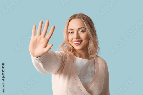 Beautiful young woman waving hand on blue background © Pixel-Shot
