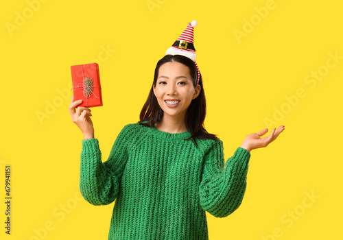 Young Asian woman in Elf hat headband with Christmas gift box on yellow background photo