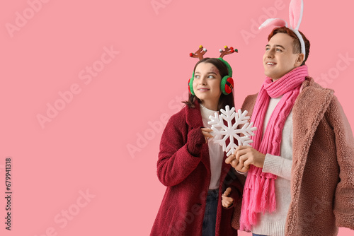 Young couple in winter clothes with snowflake on pink background