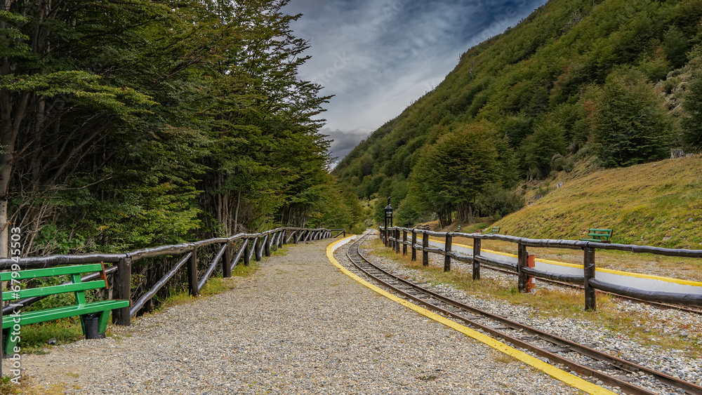 The station of the old historical narrow-gauge railway of the edge of the world. The rails, curving, disappear around the bend. A wooden fence, a bench on the side of the road. Argentina. Ushuaia.