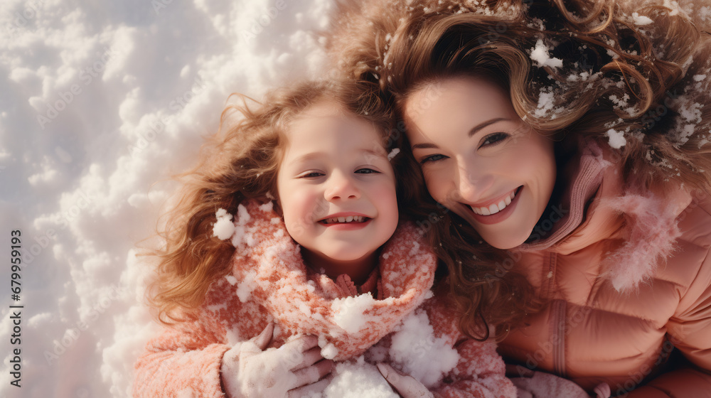 Cheerful mother and daughter having fun laying in snow outdoors in city park in winter