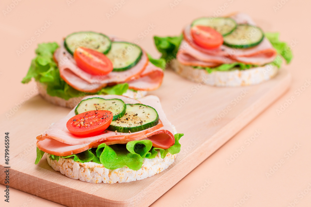 Light Breakfast. Quick and Healthy Sandwiches. Rice Cakes with Ham, Tomato, Fresh Cucumber and Green Salad on Wooden Cutting Board. Beige Background
