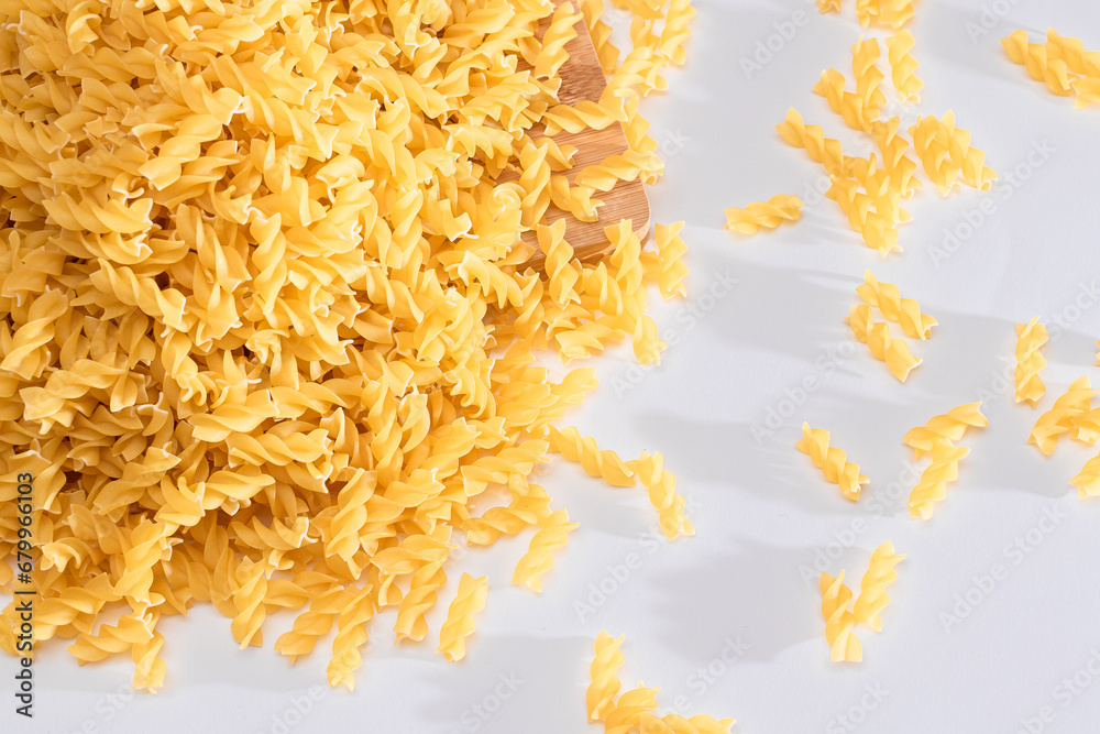 Obraz premium Uncooked Fusilli Pasta Scattered on Wooden Board and White Table. Raw and Dry Macaroni. Fat and Unhealthy Food