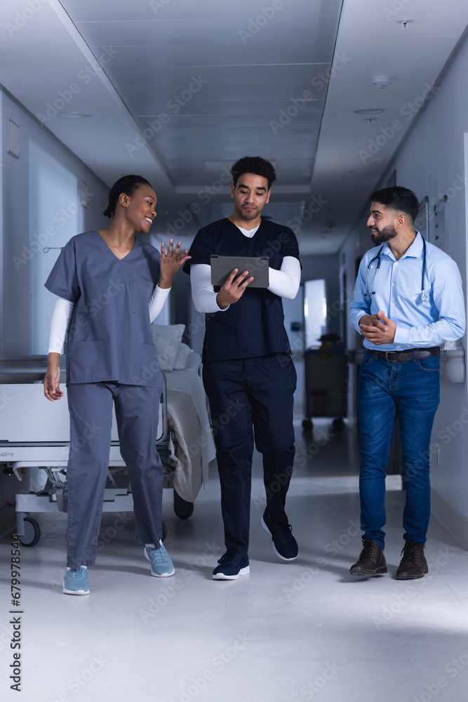 Fototapeta premium Happy diverse male and female doctors using tablet walking in hospital corridor