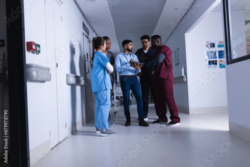 Diverse male and female doctors talking and using tablet in hospital corridor