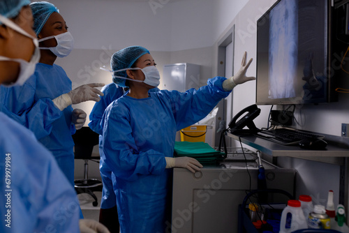 Diverse male and female doctors with face masks looking at x-rays in hospital operating room