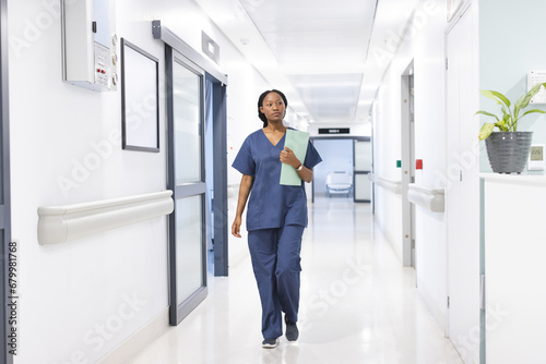 African american female doctor with documents walking in hospital corridor