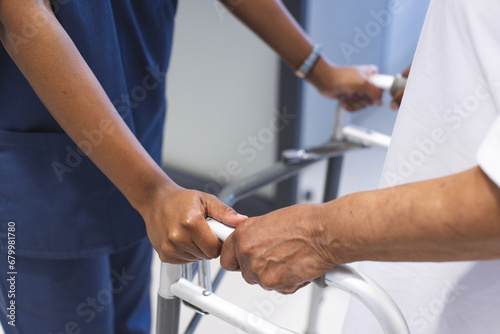 Hands of african american female doctor walking with senior female patient with crutches in hospital