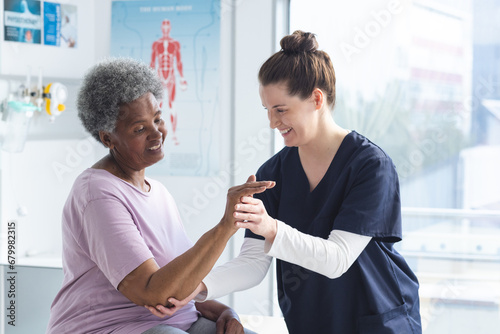 Diverse senior female patient exercising hand and female doctor advising in hospital room