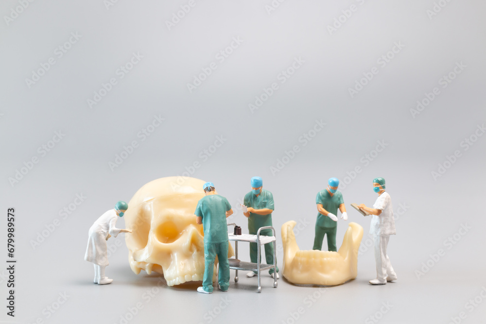 Miniature people Doctor with a giant human skull on a grey background