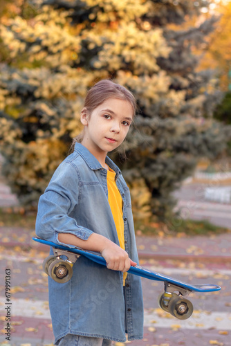 A young girl holds a skateboard in an autumn park.