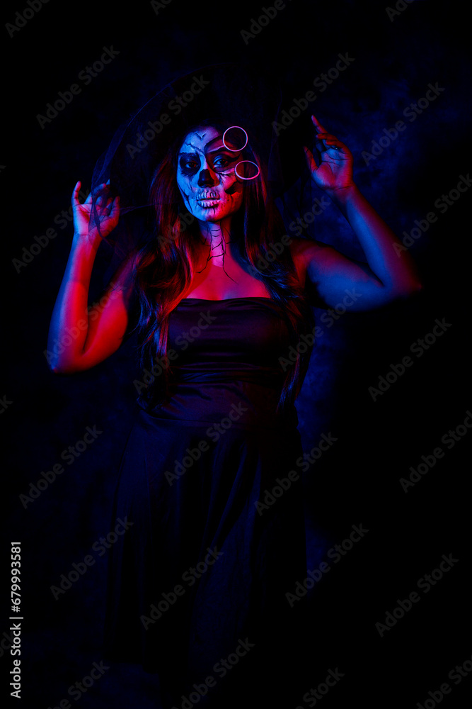 A women with Halloween Makeup in blue red light giving out a horror look wearing black gown in black background A women with Halloween Makeup in blue red light giving out a horror look wearing black gown in black background