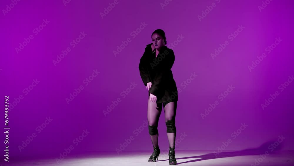 On purple background. Young woman, showing dance moves towards high heels. A spotlight beam shines on her and gives her a shadow, the edges of the background are darkened. She is sexy, rhythmic On purple background. Young woman, showing dance moves towards high heels. A spotlight beam shines on her and gives her a shadow, the edges of the background are darkened. She is sexy, rhythmic