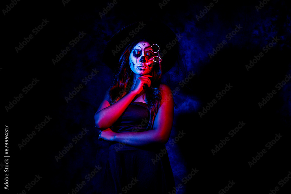 A women with Halloween Makeup in blue red light giving out a horror look wearing black gown in black background
