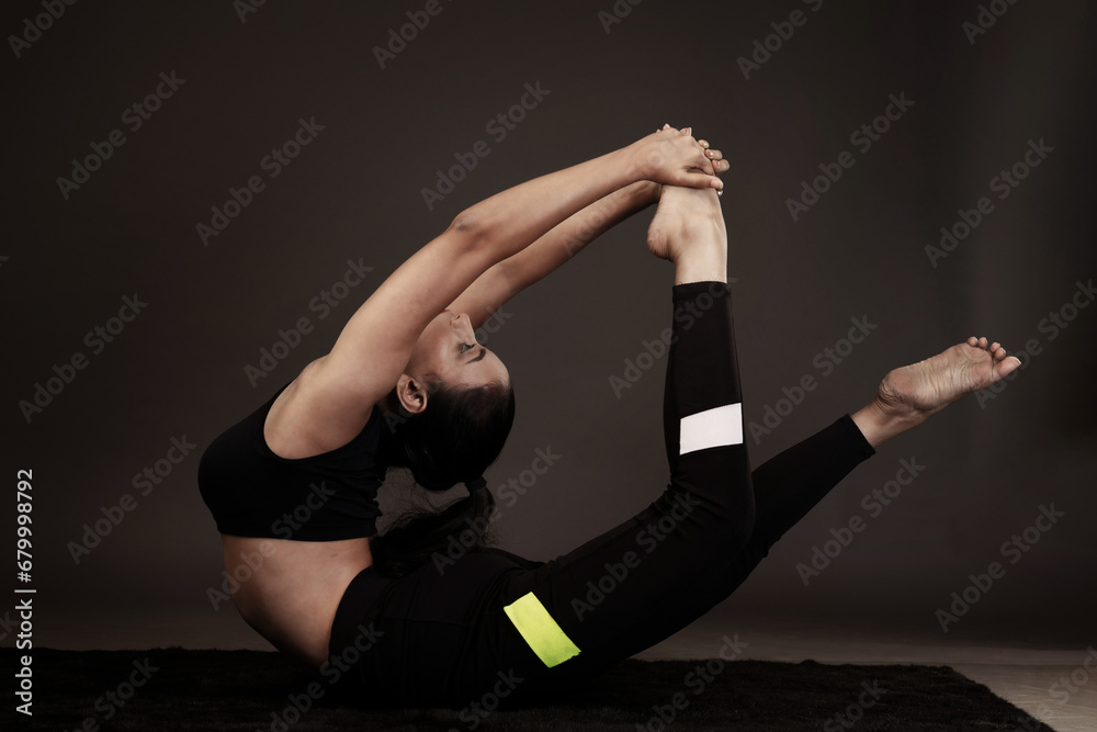 Obraz premium Slim girl performing yoga arts wearing black sports dress in black background performing yoga poses with a flexible body 