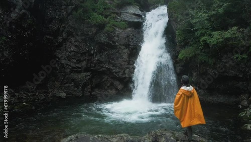 rearview of the person in yellow raincoat looks at the waterfall in forest photo