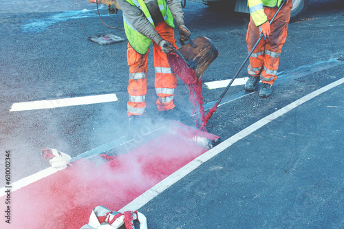 Road workers applying hot red road marking paint on new build road photo