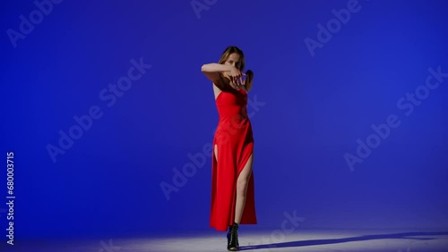 On a blue background. Young woman, showing dance moves towards high heels. A spotlight beam shines on her and gives her a shadow, the edges of the background are darkened. She is rhythmic, plastic photo