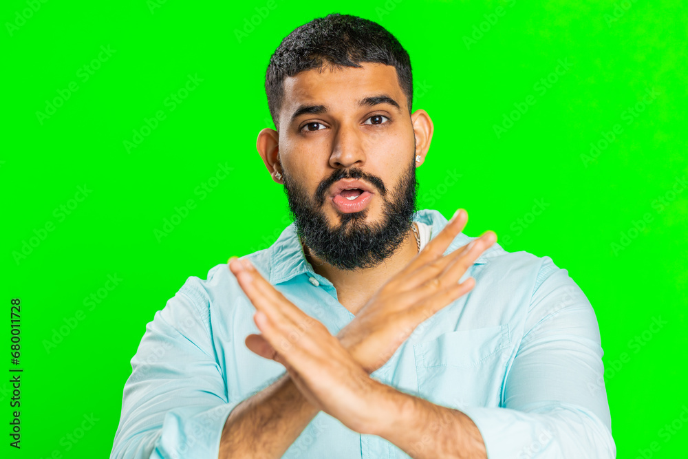 Indian young man cross hands and saying no, be careful, scolding and giving advice to avoid danger mistake, disapproval sign, disagree, dislike. Arabian guy isolated on green chroma key background Indian young man cross hands and saying no, be careful, scolding and giving advice to avoid danger mistake, disapproval sign, disagree, dislike. Arabian guy isolated on green chroma key background