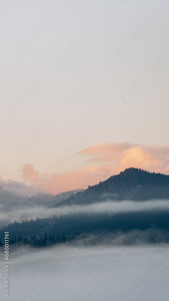 Photo of a picturesque landscape overlooking mountain forests. Dawn in the mountains. Fog covering everything around. Travel to quiet and serene places. Can be used as banner background, wallpaper.