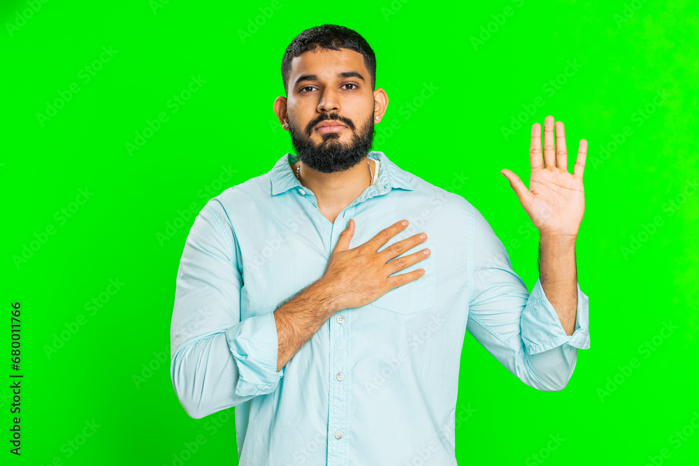 I swear to be honest. Sincere responsible Indian man raising hand to take oath, promising to be honest, to tell truth, keeping hand on chest, justice. Guy isolated on green chroma key background I swear to be honest. Sincere responsible Indian man raising hand to take oath, promising to be honest, to tell truth, keeping hand on chest, justice. Guy isolated on green chroma key background