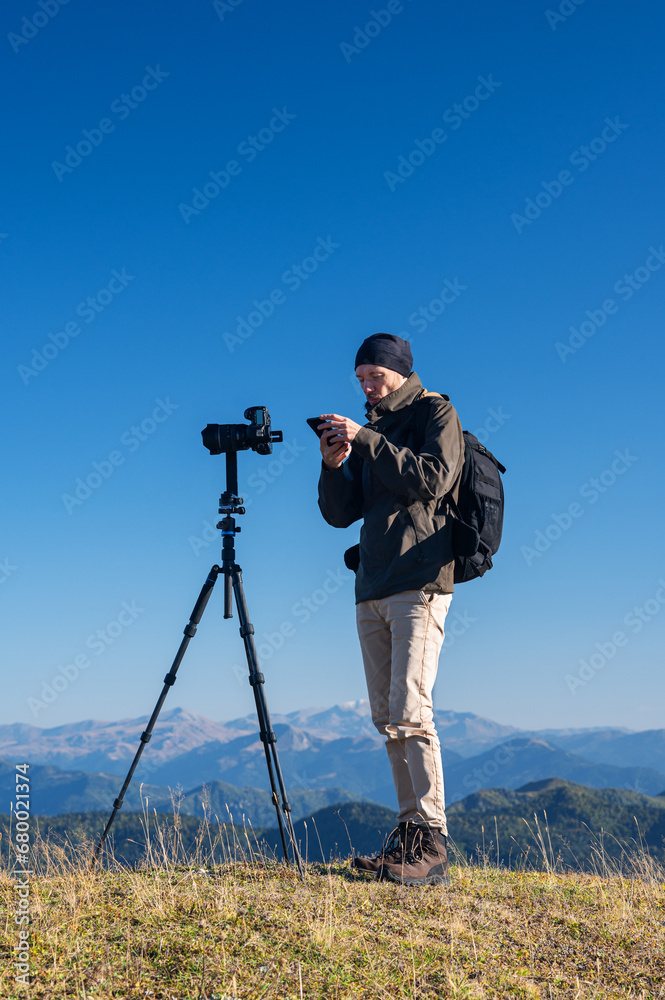 A photographer takes a photo of a beautiful mountain landscape with colorful trees and snow peaks on a sunny autumn day. Traveling through the mountains of Georgia.