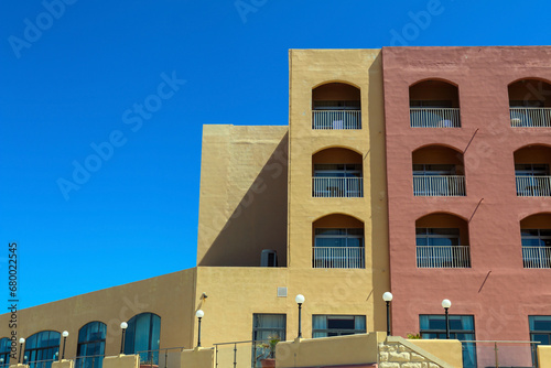 Colourful holiday resort apartment block, vivid yellow and blush red building with arched balconies and clear blue sky if a copy space needed.